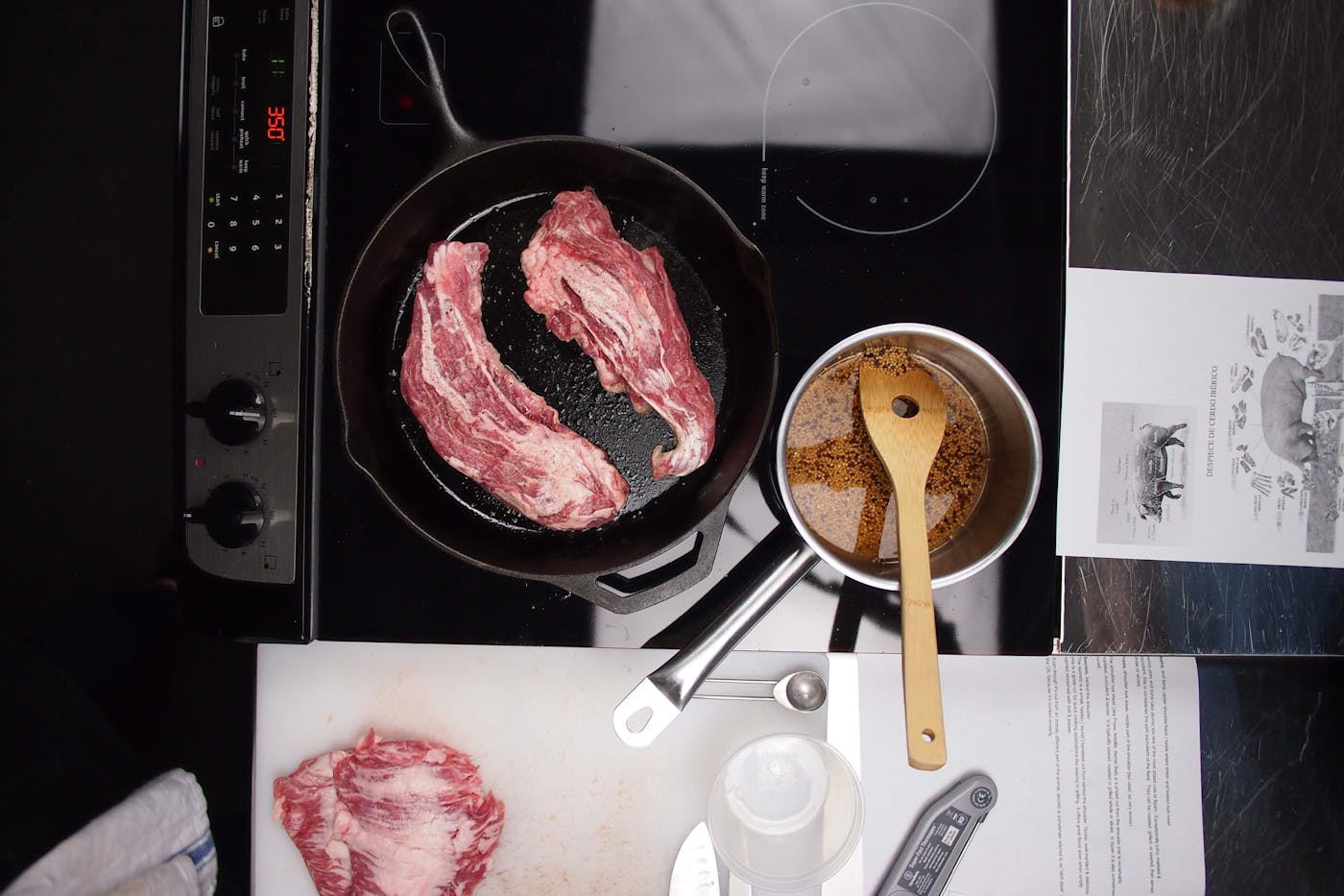 Two Iberico Secreto cuts cooking in a cast iron skillet next to mustard seeds and recipe notes